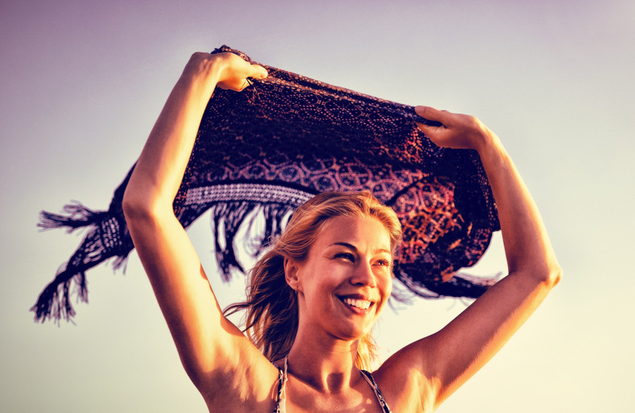 Happy woman holding scarf against clear sky